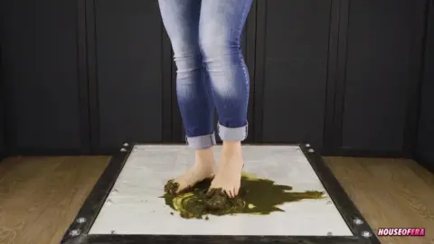 Slim blonde in jeans steps on and stands in feces barefoot on white pl